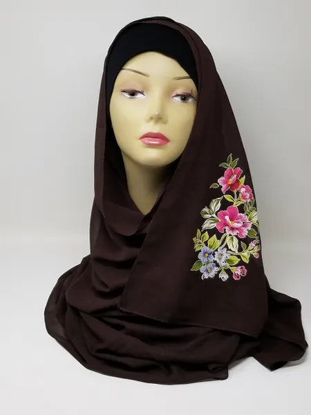 Dark brown hijab scarf with colorful floral print on the side displayed on mannequin, modest Muslim headscarf for women, elegant floral hijab wrap for everyday modest fashion and Islamic clothing.