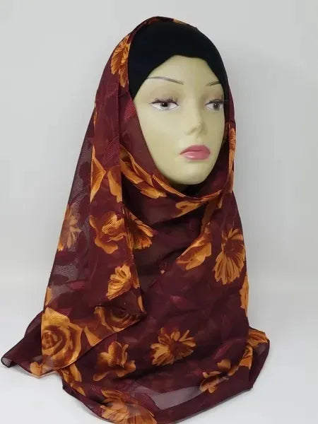 Burgundy floral georgette hijab draped on mannequin, lightweight breathable scarf with gold leaf pattern, soft textured matte fabric, flowy elegant modest head covering for women, stylish hijab for everyday wear and special occasions
