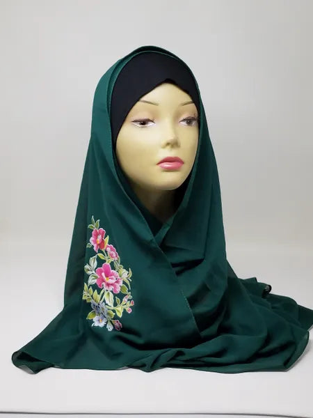 Dark green hijab scarf with colorful floral print on the side displayed on mannequin, modest Muslim headscarf for women, elegant green hijab wrap for everyday modest fashion and Islamic clothing.