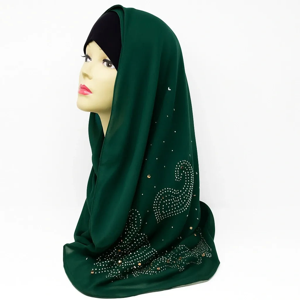 Emerald green chiffon hijab with rhinestone embellishments draped on mannequin, elegant modest fashion scarf for Muslim women, lightweight breathable chiffon headscarf perfect for Eid, weddings, and everyday wear