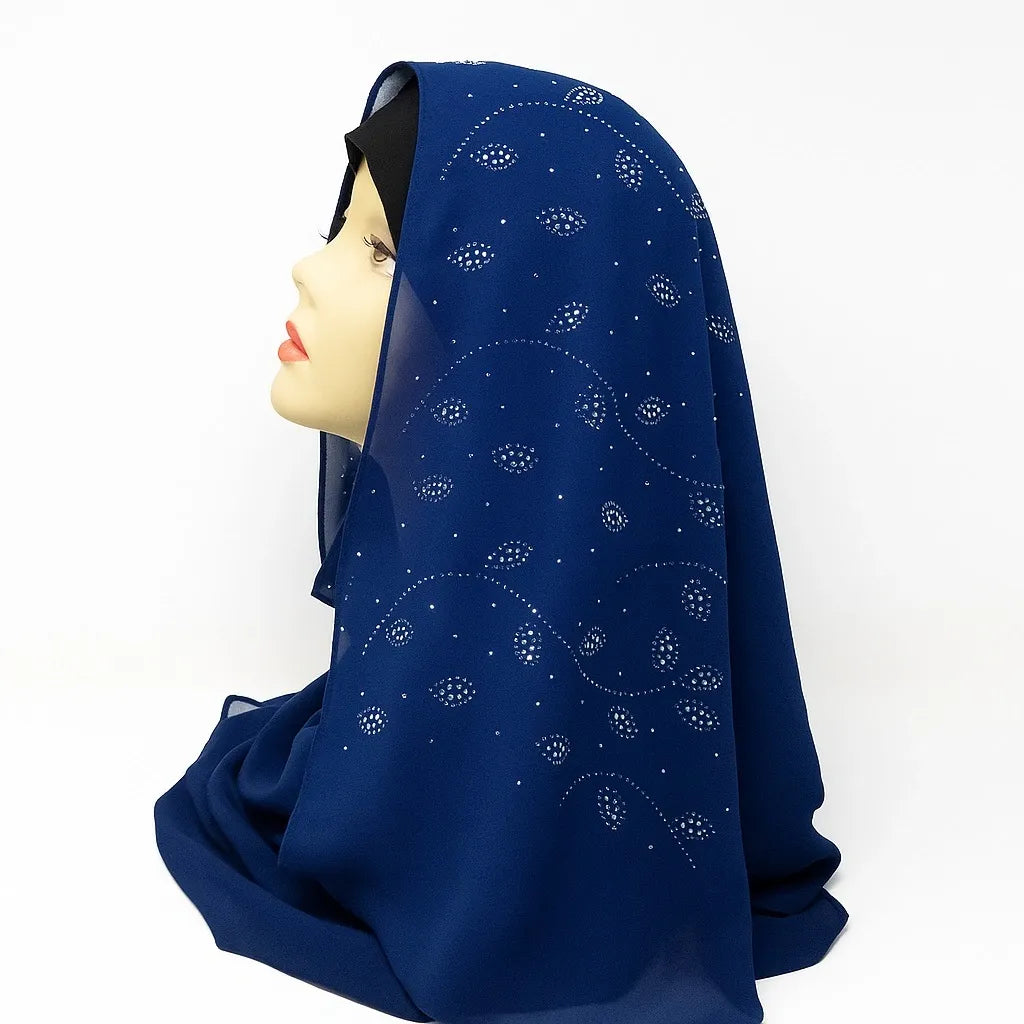 Navy blue chiffon hijab with rhinestone embellishments draped on mannequin, elegant modest fashion scarf for Muslim women, lightweight breathable chiffon headscarf perfect for Eid, weddings, and everyday wear.