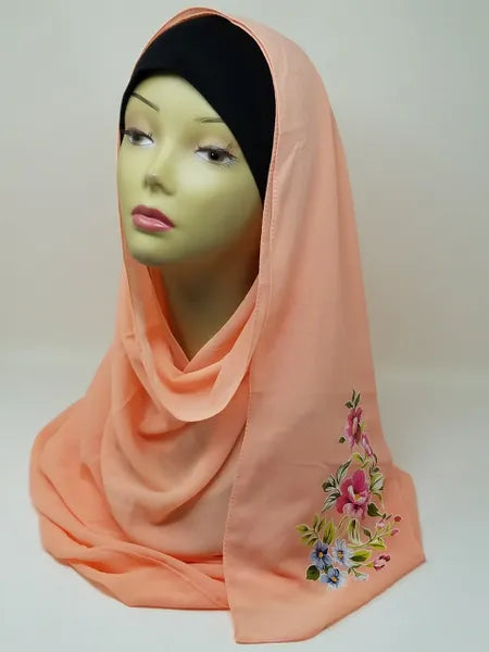 Peach hijab scarf with colorful floral print on the side displayed on mannequin, modest Muslim headscarf for women, elegant peach hijab wrap for everyday modest fashion and Islamic clothing.