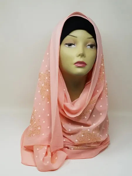 Peach chiffon hijab scarf with polka dot texture and gold flower accents, elegant lightweight modest fashion headscarf draped on mannequin, perfect for weddings, special occasions, and stylish everyday hijab wear.