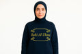 Woman wearing black Islamic long sleeve shirt with gold “Rabi Al-Thani” text design, modest Muslim apparel on wWoman wearing black Islamic long sleeve shirt with gold “Rabi Al-Thani” text design, modest Muslim apparel on white backgroundhite background