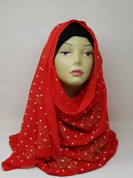 Red chiffon hijab scarf with gold polka dot pattern displayed on mannequin head, lightweight modest fashion headscarf with soft drape perfect for everyday wear, special occasions, and elegant hijab styling.